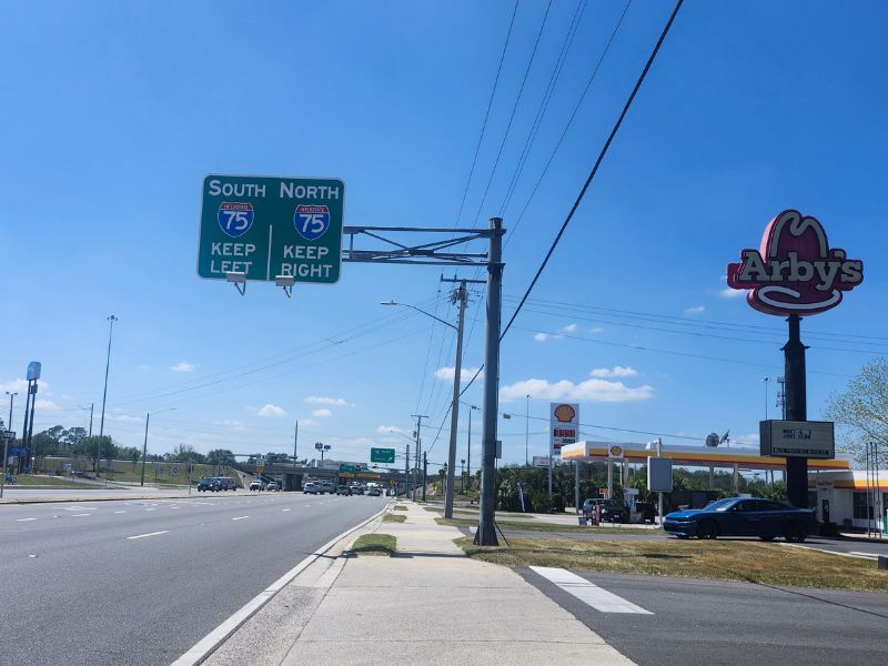 You said
alt text for the image
Gemini said
A sunny, wide-angle view of a main road in Lake City, Florida, showing the Interstate 75 South and North directional signs under a clear blue sky. To the right, the iconic tall Arby's hat sign stands near a Shell gas station, representing the modern commercial gateway that contrasts with the region's historic cattle ranching roots.